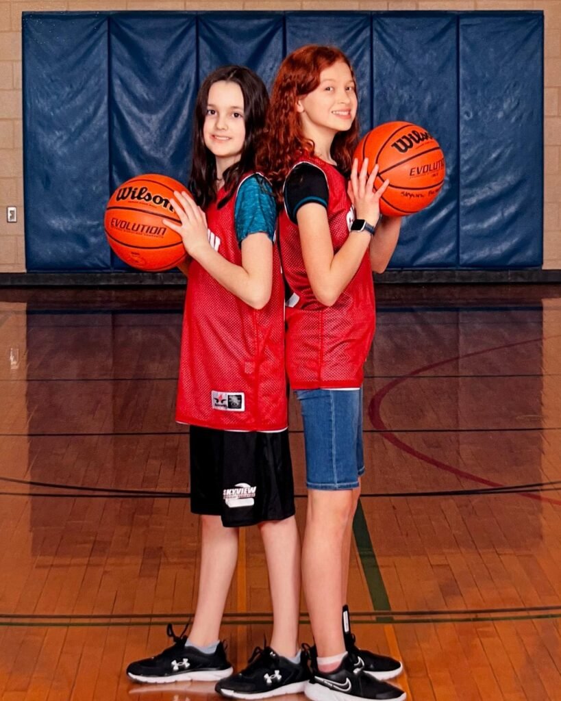 Two basketball players in red jerseys pose back-to-back with Wilson basketballs on a wooden court. A second image shows a close-up of a player smiling with a ball, highlighting athletic shoes on the polished gym floor.
