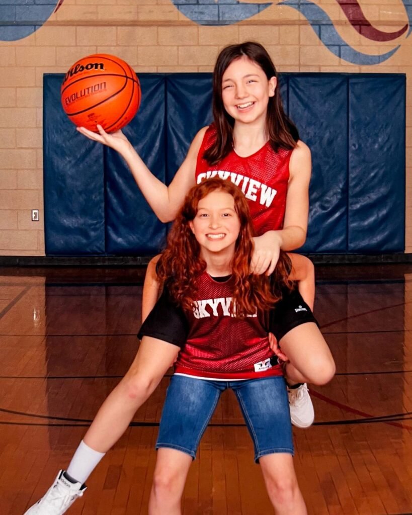 Two basketball players in red Marryview jerseys posing for a cutie photo on the gym floor.