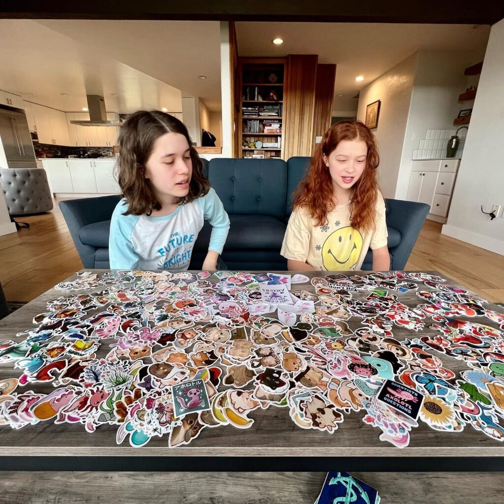 Children sit at a living room table filled with a wide collection of colorful stickers.