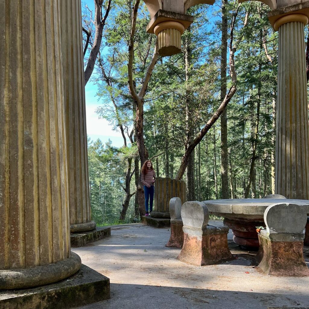 A historic stone observation pavilion surrounded by the Pacific Northwest forest. Pillars and stone furniture offer a serene setting for travelers to enjoy the surrounding nature.