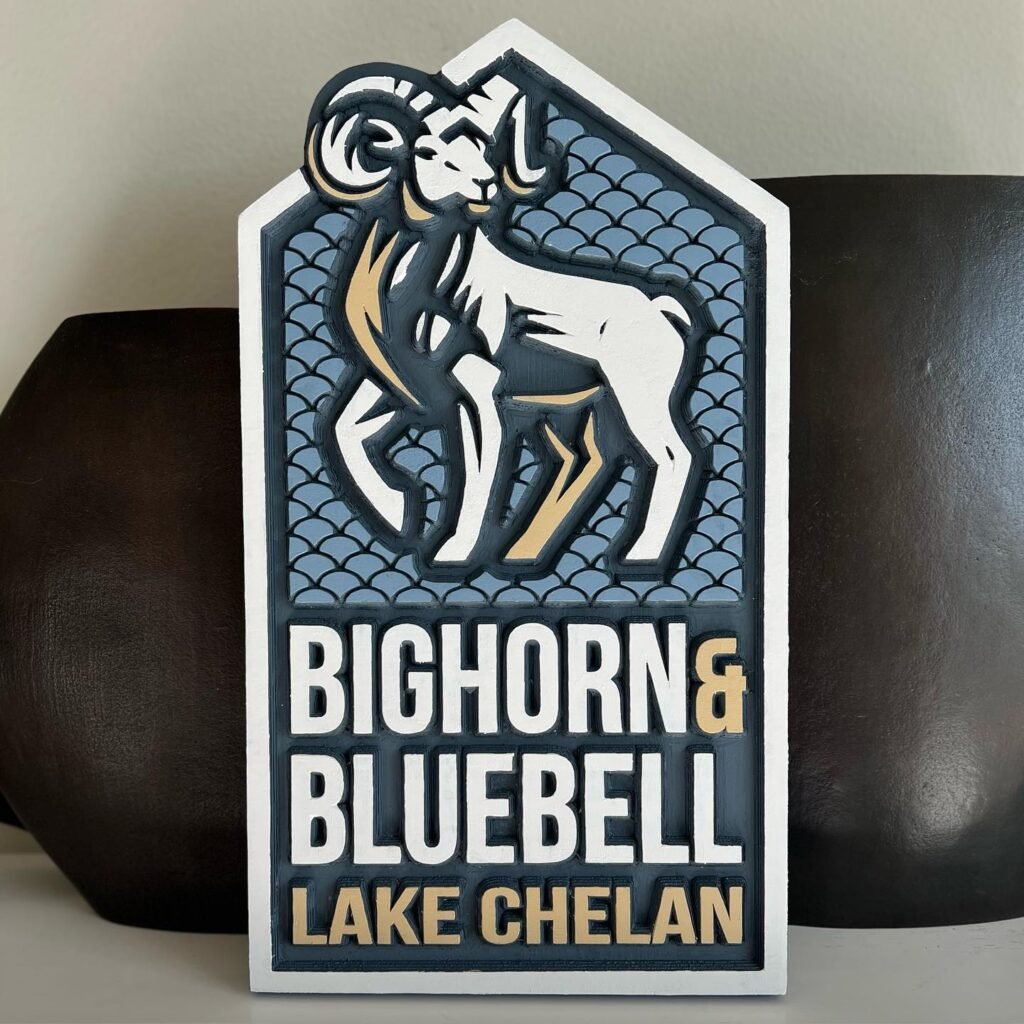 A decorative sign featuring a stylized bighorn ram on a textured blue background with the text Bighorn & Bluebell Lake Chelan.