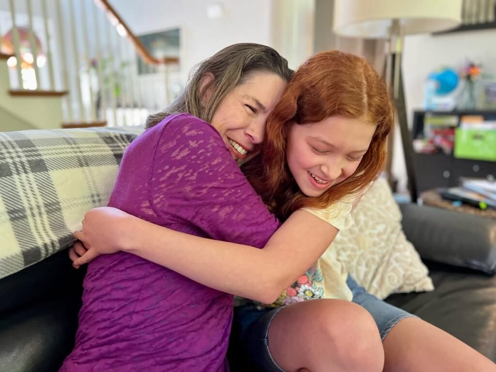 Two individuals share a warm hug on a couch in a cozy living room setting.