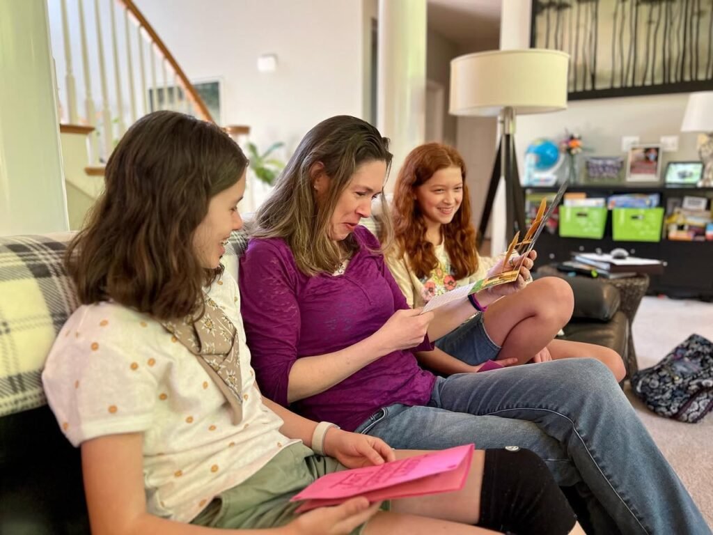 Three people reading a book together on a couch in a cozy home.