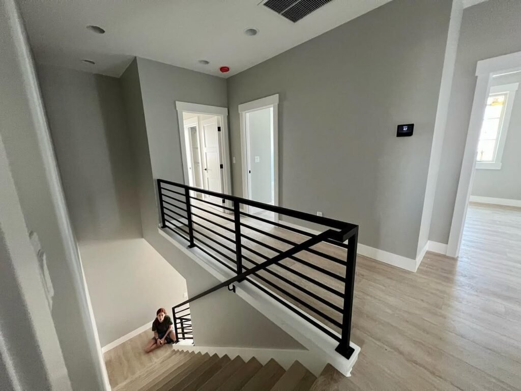 A view over a modern black metal railing on a staircase with light wood flooring and gray walls.