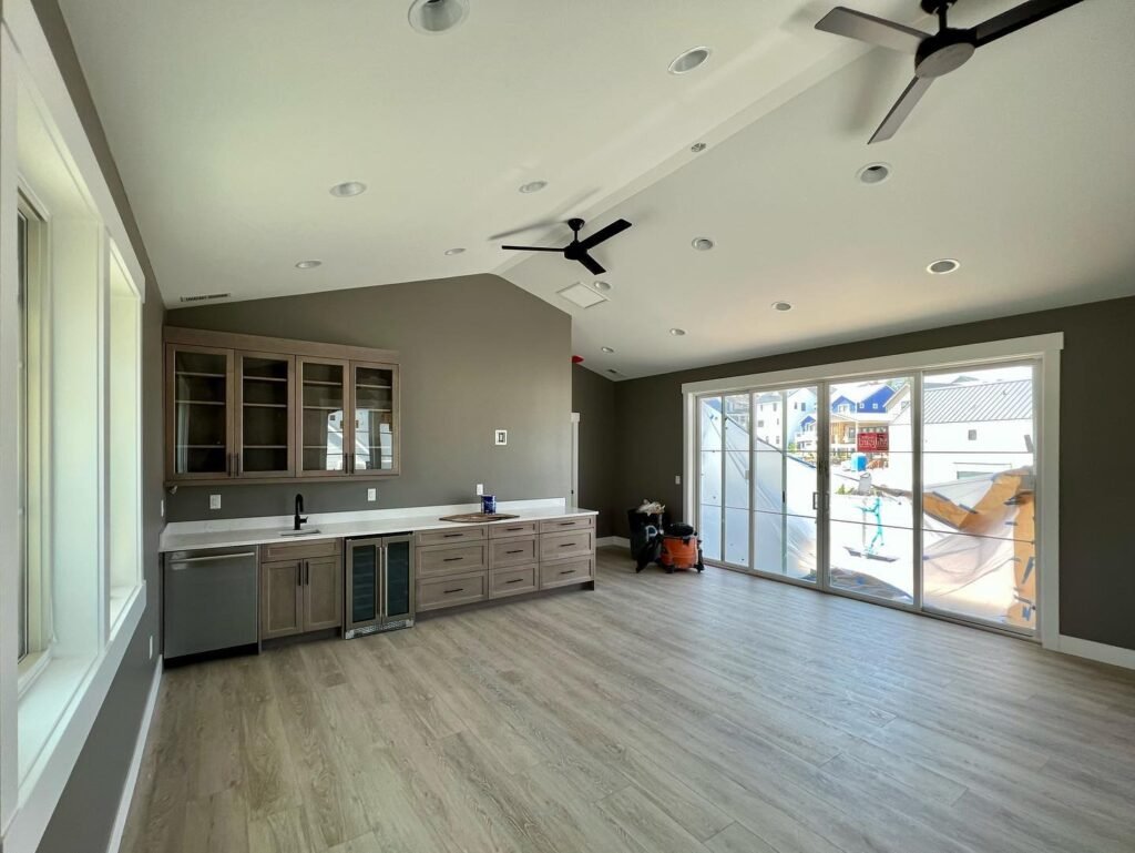 A large kitchen area with gray cabinetry and light wood-style flooring. The space includes ceiling fans and access to an outdoor area.