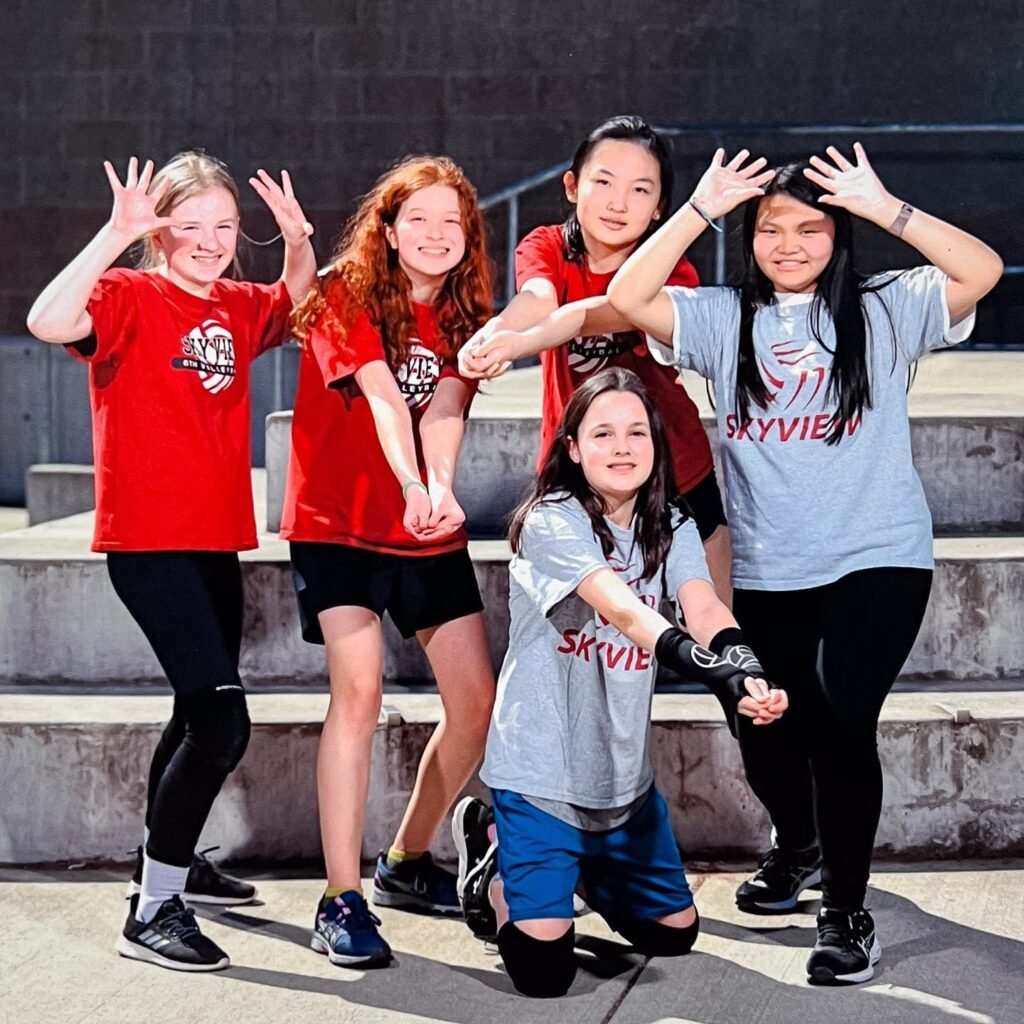 A group of five young people in matching team shirts posing outdoors.