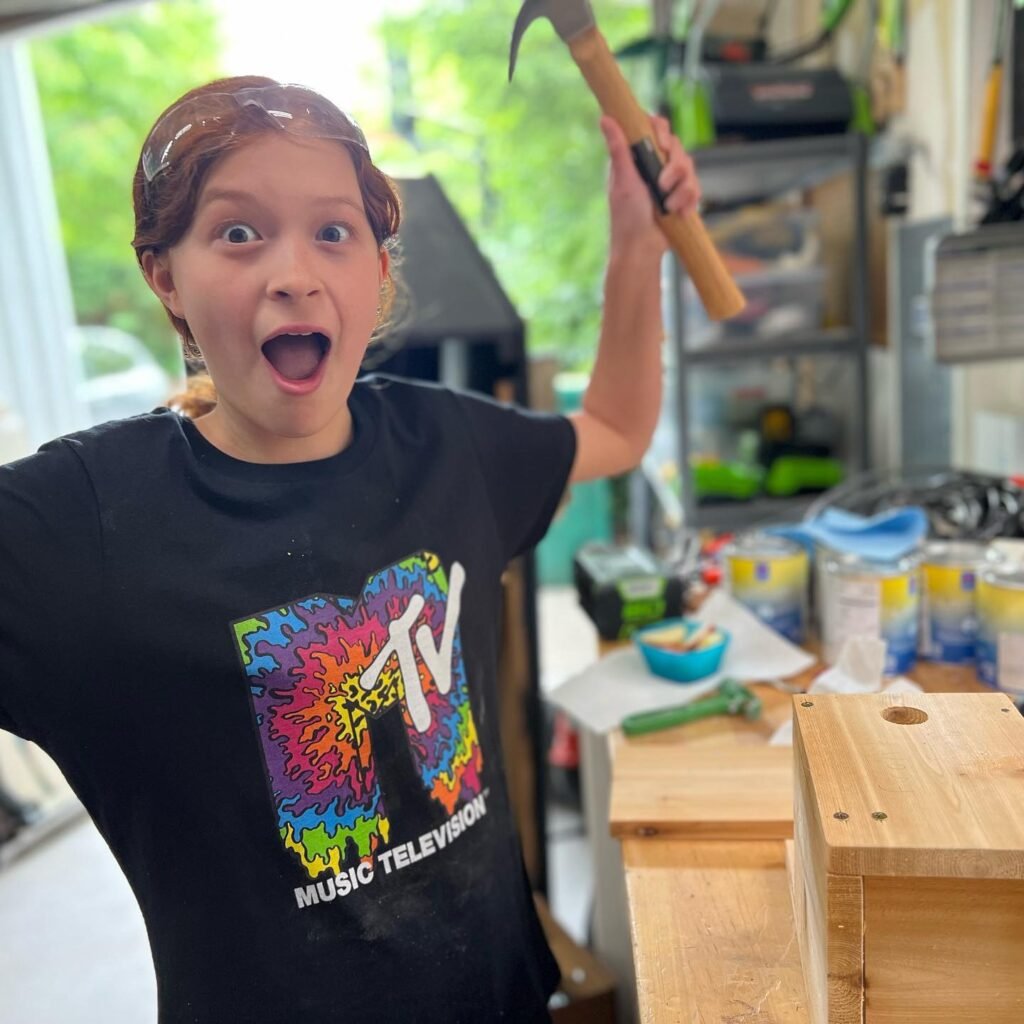 A person holding a mallet with an excited expression in a home workshop.