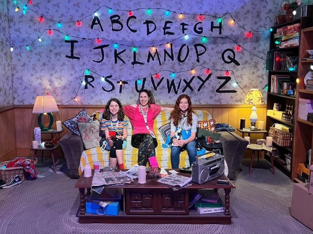 Three people watching a movie in a cozy living room with hand-drawn alphabet wall art.