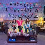 Three people watching a movie in a cozy living room with hand-drawn alphabet wall art.