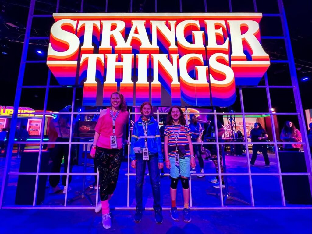 A group standing in front of a large, illuminated Stranger Things logo at a themed event.