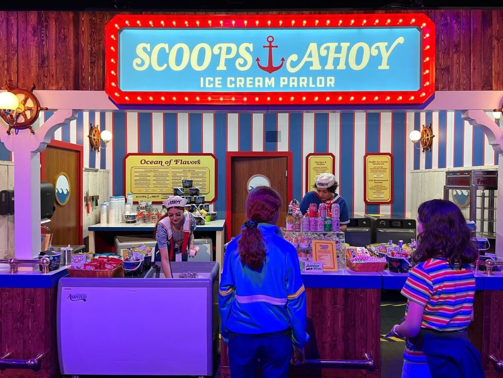 Colorful view of the Scoops Ahoy Ice Cream Parlor sign and storefront. Visitors enjoy a lively scene at this themed attraction.