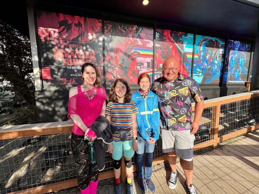 Four individuals pose together in front of colorful abstract murals and a wooden railing at an outdoor urban gallery.