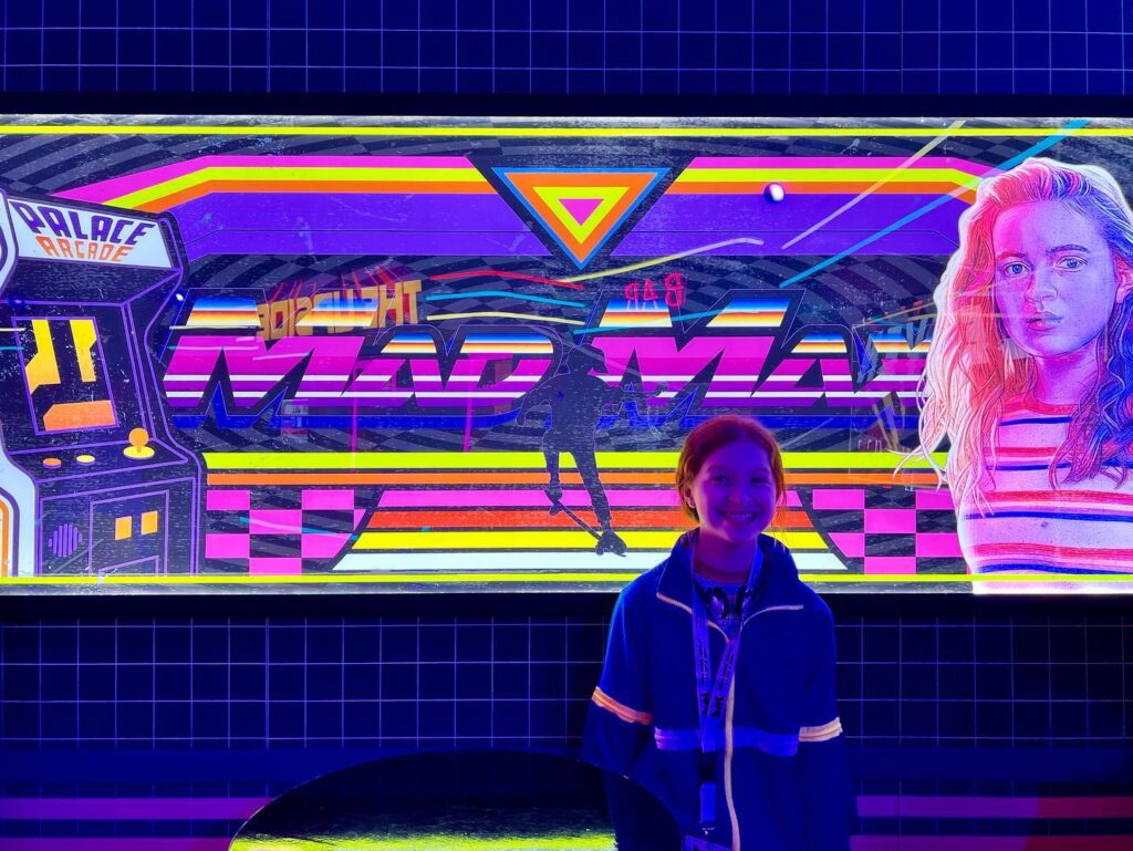 A colorful neon vaporwave artwork featuring geometric shapes, a grid, and a retro arcade machine.