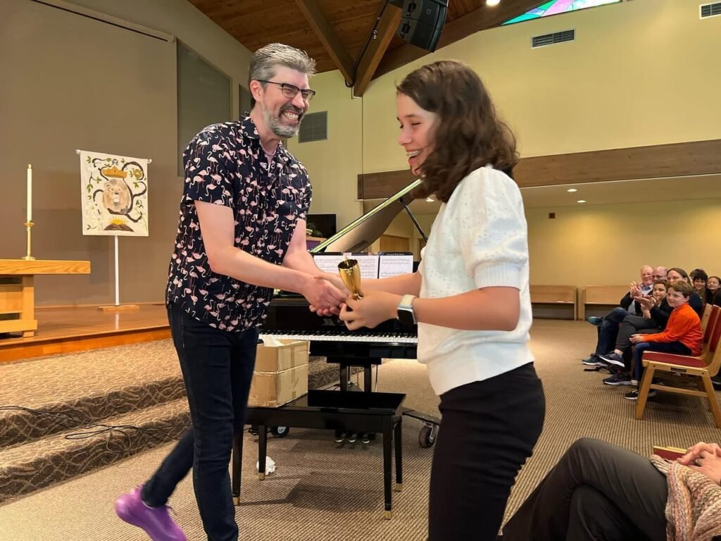 A performer receives a trophy from another individual during a piano recital in a church hall.