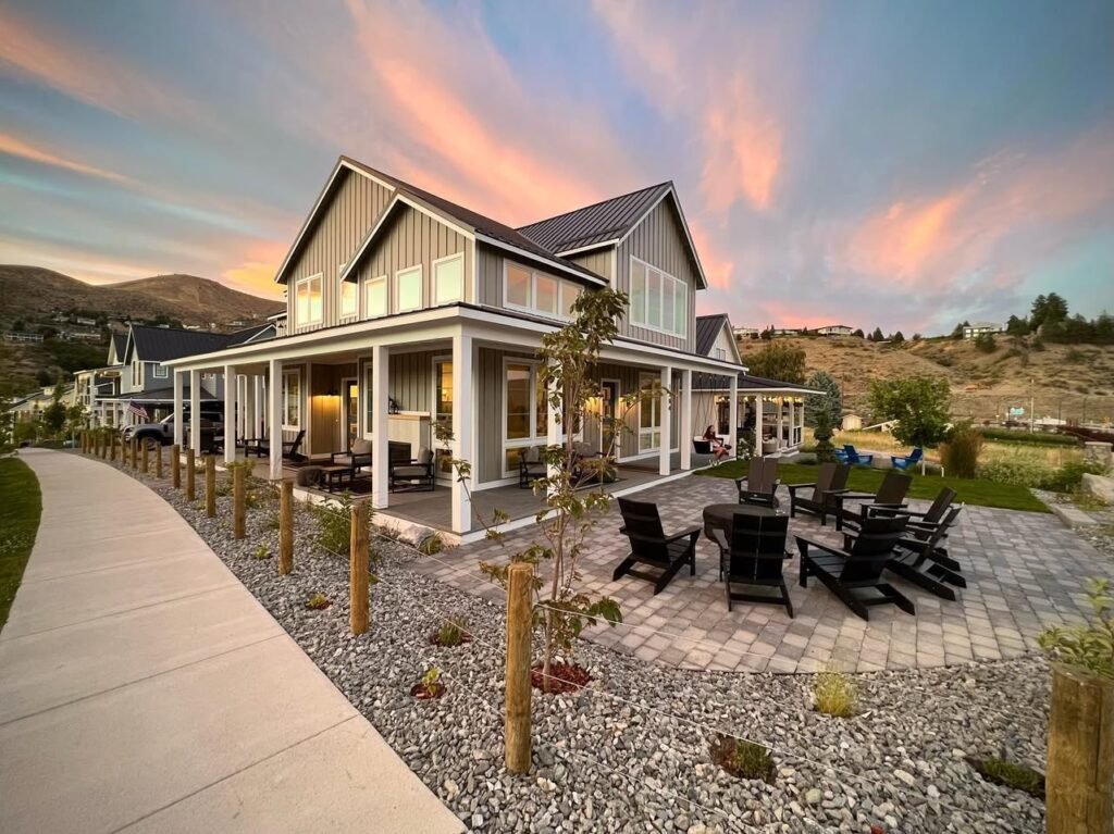 A stunning coastal retreat with a wraparound porch, set against a vibrant sunset sky and rolling hills. The home features modern design elements and a well-maintained landscape.