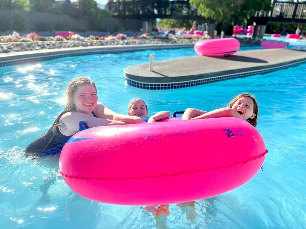 Three people floating on a pink flamingo float in a bright blue pool.