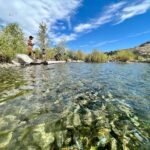 Snake Charmer Panoramic collage of a clear river with rocky banks, bright blue skies, and green foliage under sunny conditions.