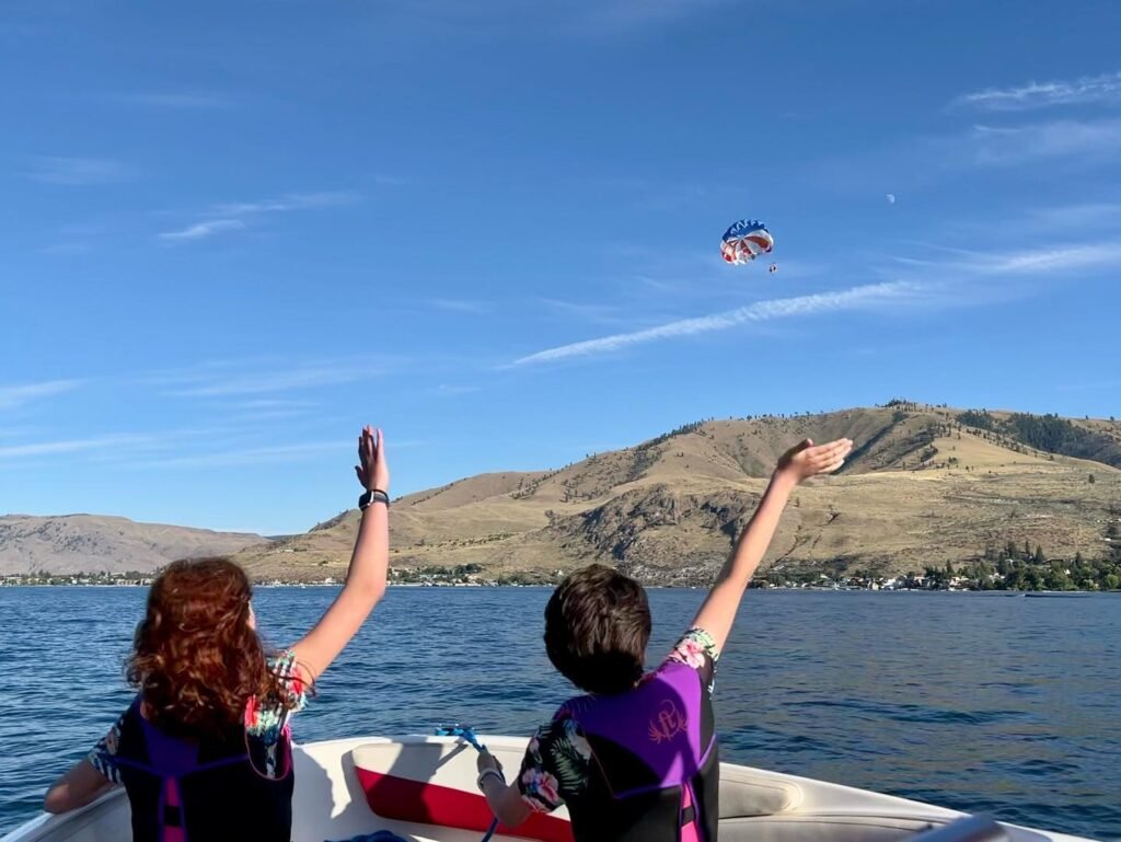 View from a boat in Lake Okataina, Taupo, New Zealand, looking towards the hills with a parachute in the sky.