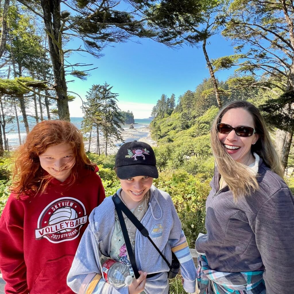 A family enjoying a sunny day outdoors with a scenic coastal view and lush evergreen trees in the background.