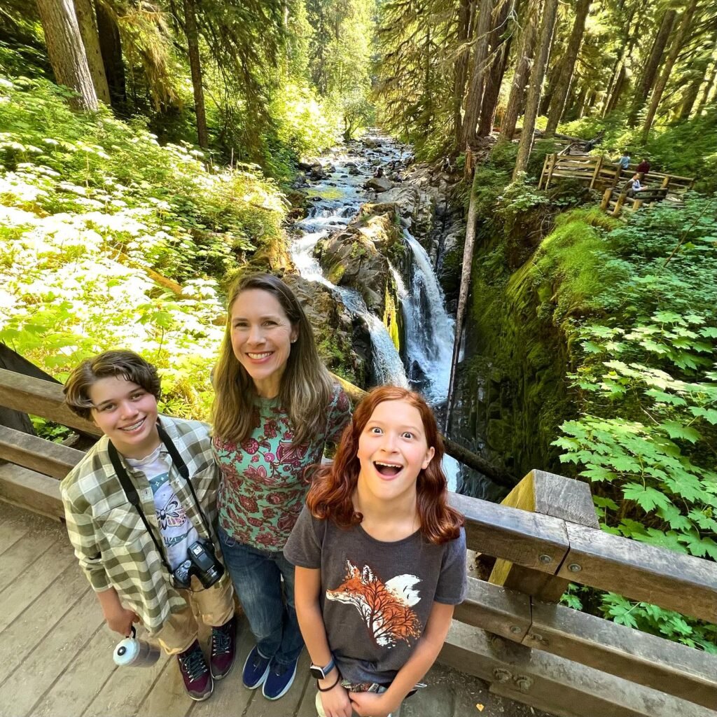 A family enjoys a hike alongside Crystal Falls, surrounded by dense Pacific Northwest forest and white waterfalls.