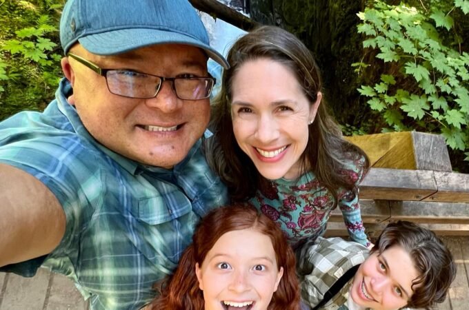 A family takes a selfie together in front of a waterfall and lush greenery. The group is smiling and enjoying their time outdoors.