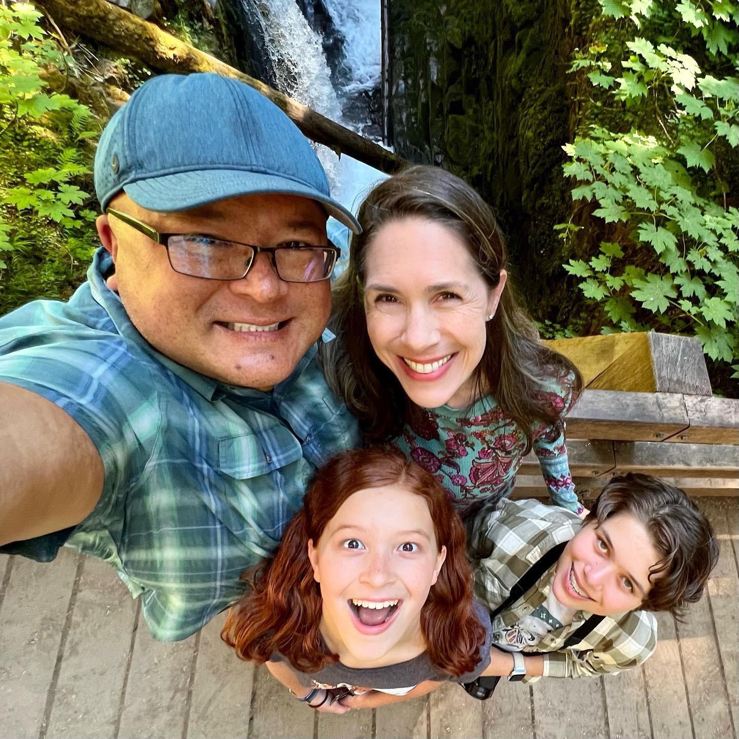 Sol Duc A family takes a selfie together in front of a waterfall and lush greenery. The group is smiling and enjoying their time outdoors.