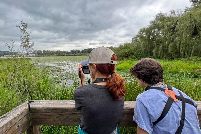 Two people overlooking a lush wetland while one captures photos.