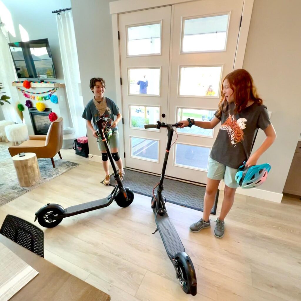 Two people standing with electric scooters in a home.