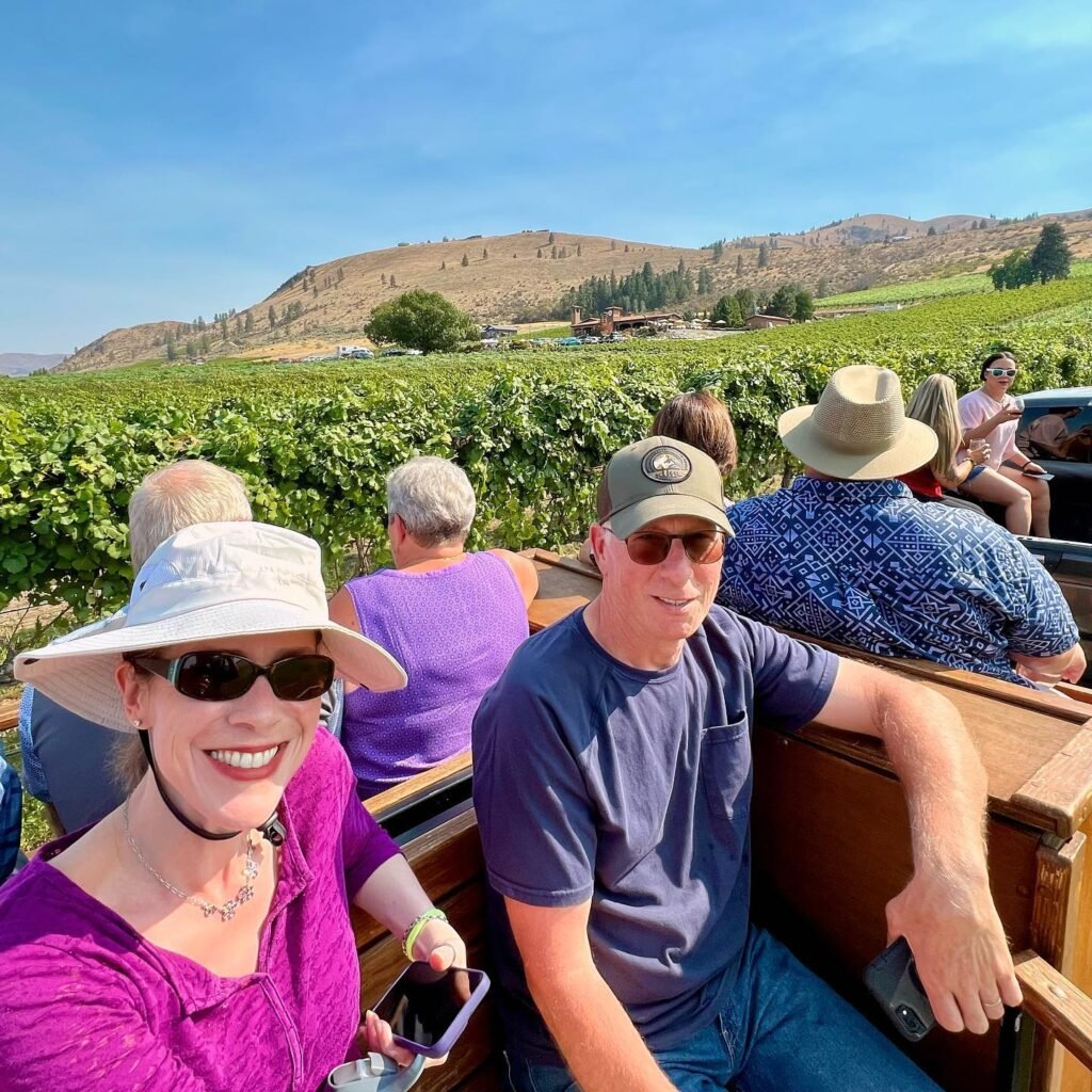 A couple taking a selfie on a convertible tour vehicle surrounded by lush vineyards and rolling hills.