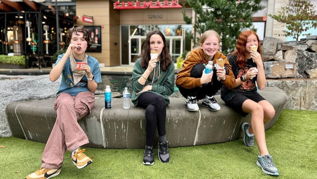 A family of four enjoys together ice cream cones on a stone bench outdoors, capturing a relaxed and happy moment during a trip in the Pacific Northwest.