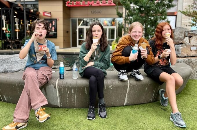 A family of four enjoys together ice cream cones on a stone bench outdoors, capturing a relaxed and happy moment during a trip in the Pacific Northwest.