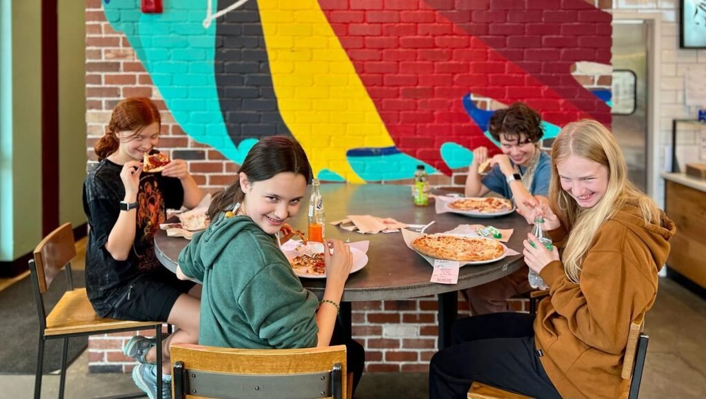 A group of friends sharing a meal around a table with a vivid, colorful mural in the background.