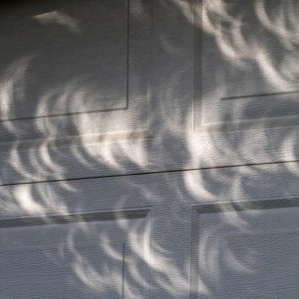 Abstract close-up of sunlight filtering through grasses to create fluted light patterns on gray wooden siding.