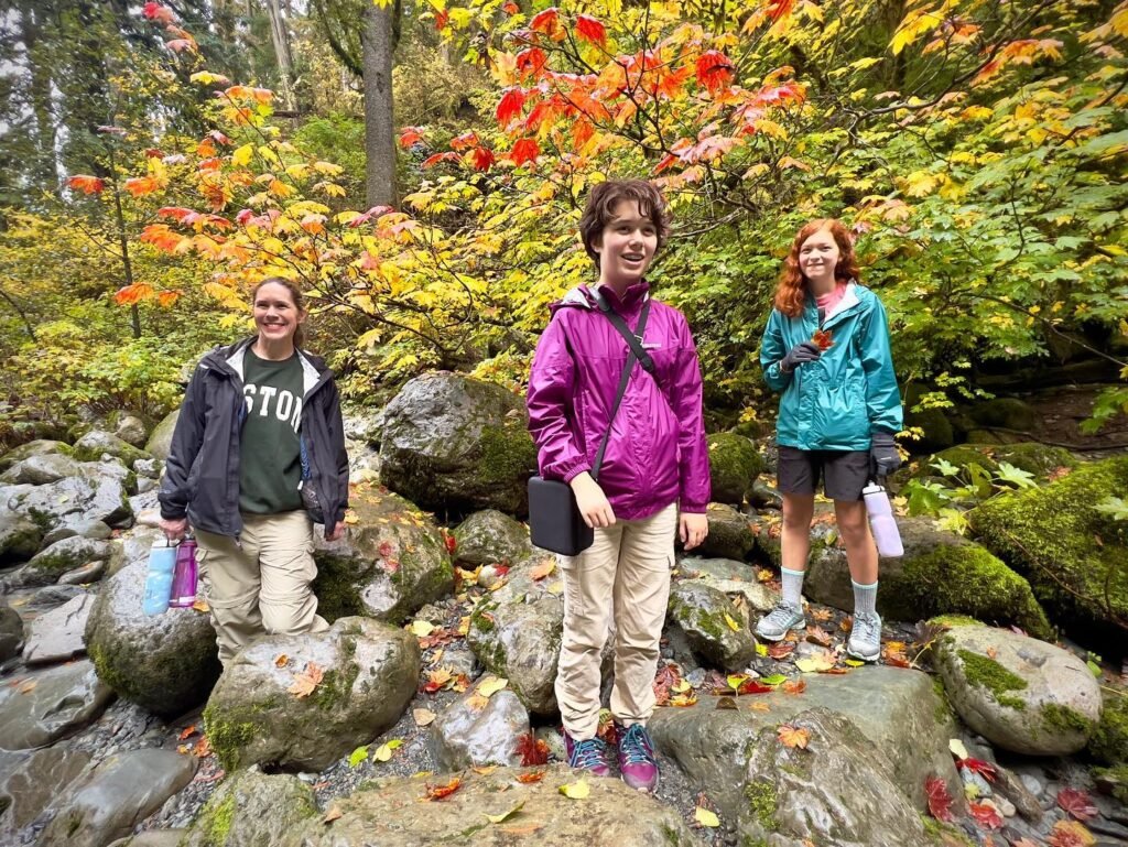 Three friends pose among large mossy rocks and vibrant autumn forest foliage.