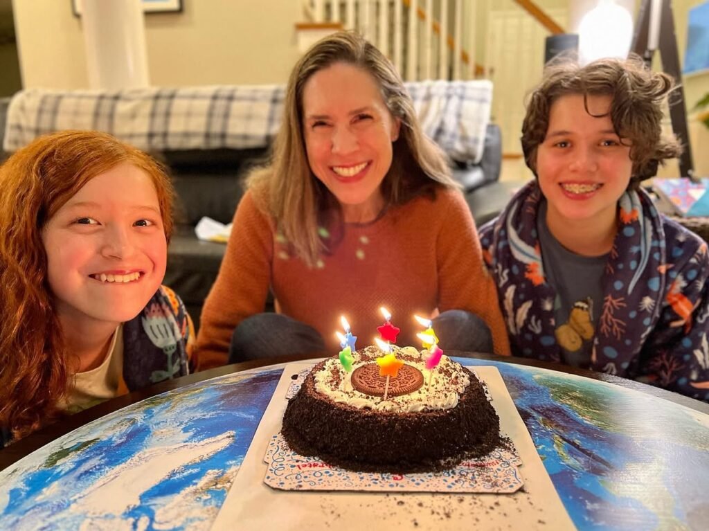 A family smiles together for a birthday photo with a chocolate cake with lit candles on the table.