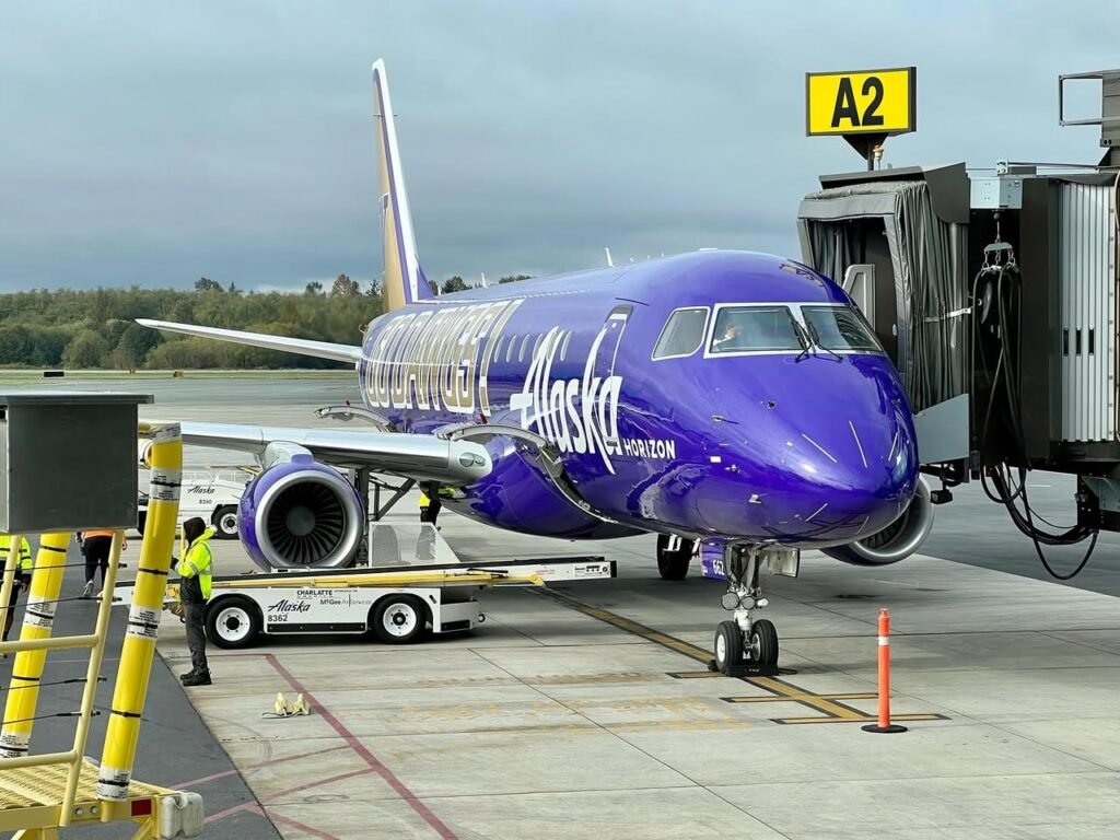 An Alaska Airlines aircraft parked at airport gate A2 under an overcast sky.