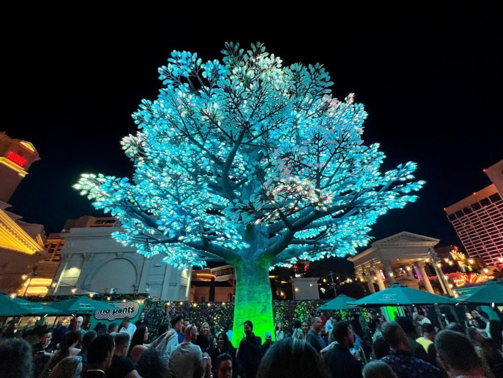 The iconic glowing bonsai trees at Wynn Las Vegas illuminated in vibrant blue and green lights with a crowd below.
