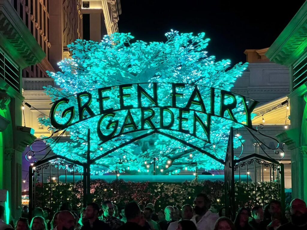 An illuminated tree and sign spelling out Green Fairy Garden at night.