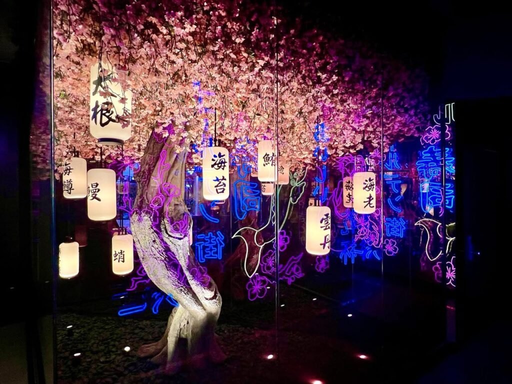 Glowing lanterns and cherry blossoms illuminate an indoor diorama at a traditional Japanese festival.