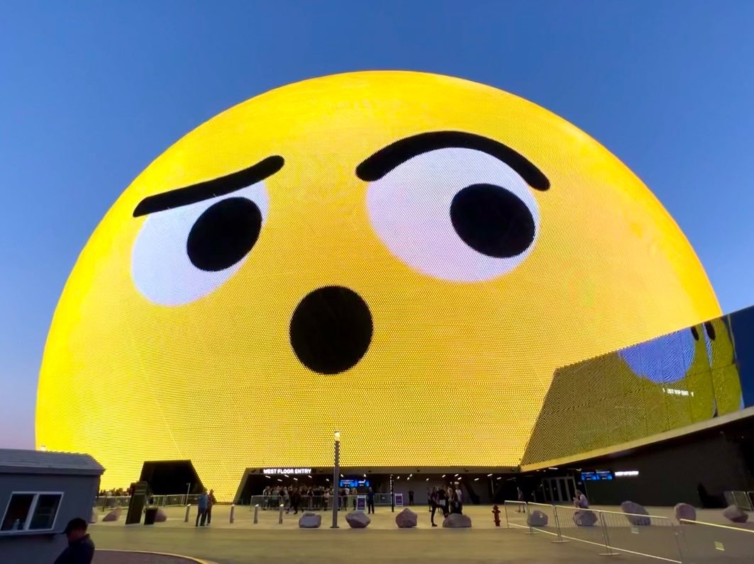 Las Vegas A large yellow surprised emoji displayed on a building facade at night. A close-up of the emoji's expressive eyes and raised eyebrows.