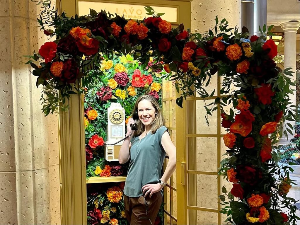 A vibrant floral arch adorns the entrance of the Fogo restaurant lobby, with a woman holding a microphone in front of the colorful blooms.