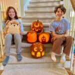 Children smiling beside lit jack-o-lanterns on a staircase.