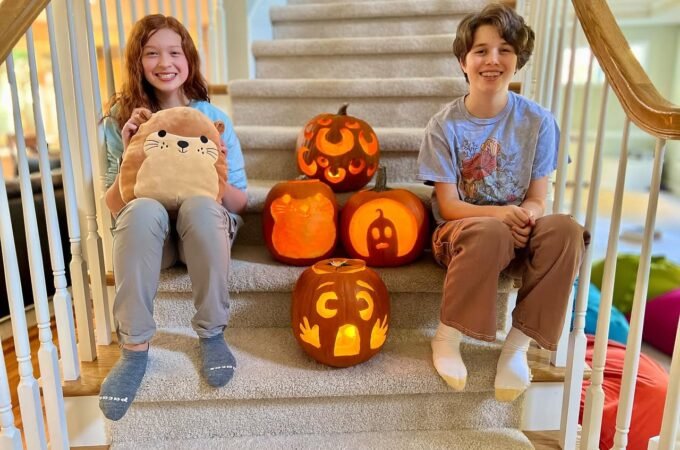 Children smiling beside lit jack-o-lanterns on a staircase.