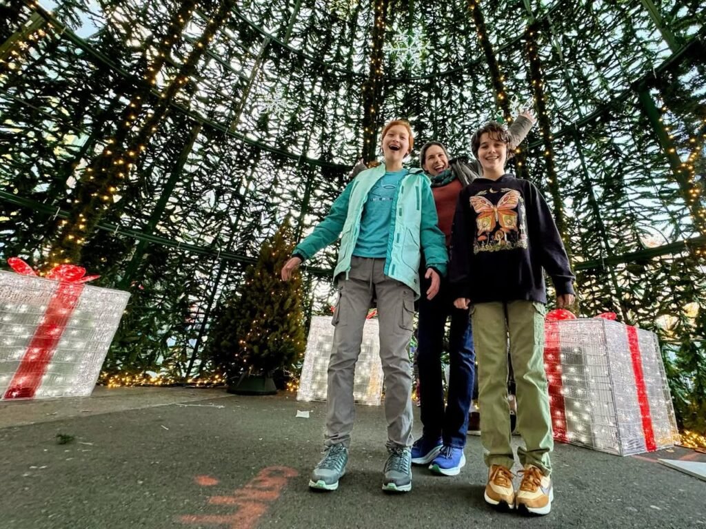 A group enjoys a festive moment beneath a huge, illuminated pine tree at a holiday event.