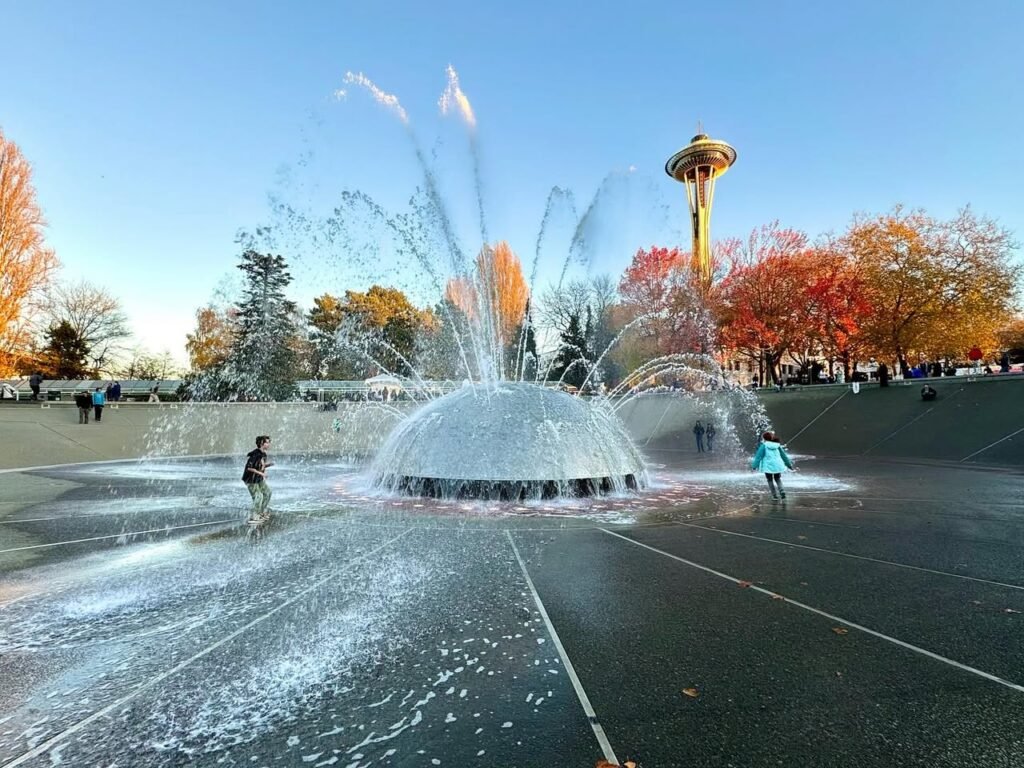 A splashy fountain plaza in Seattle with the Space Needle featuring vibrant autumn foliage and playful water.