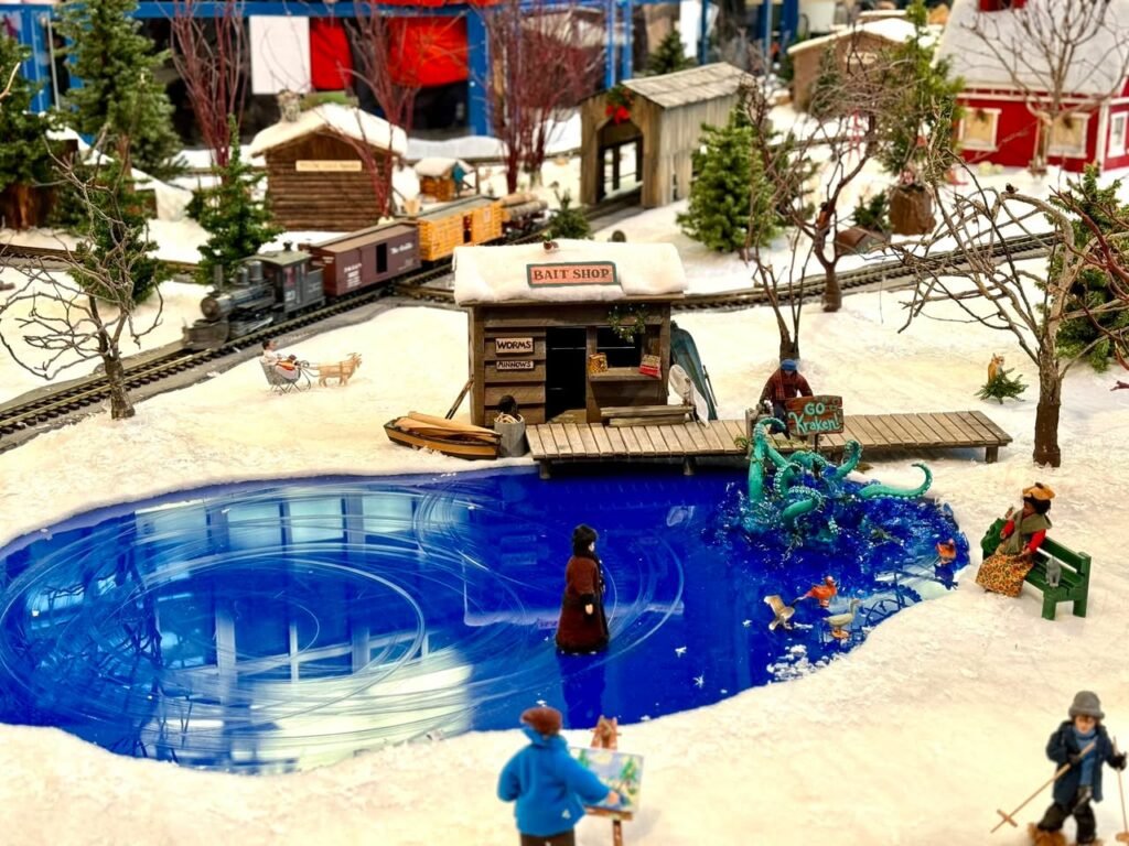 A charming model of a snowy winter scene featuring a vibrant ice skating rink, a small wooden station, and intricate surrounding village details.
