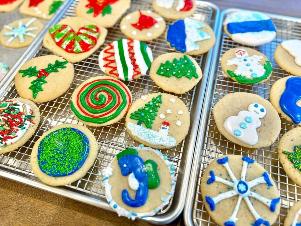 Two trays of decorated shortbread cookies featuring maritime, holiday, and coastal designs on a cooling rack.