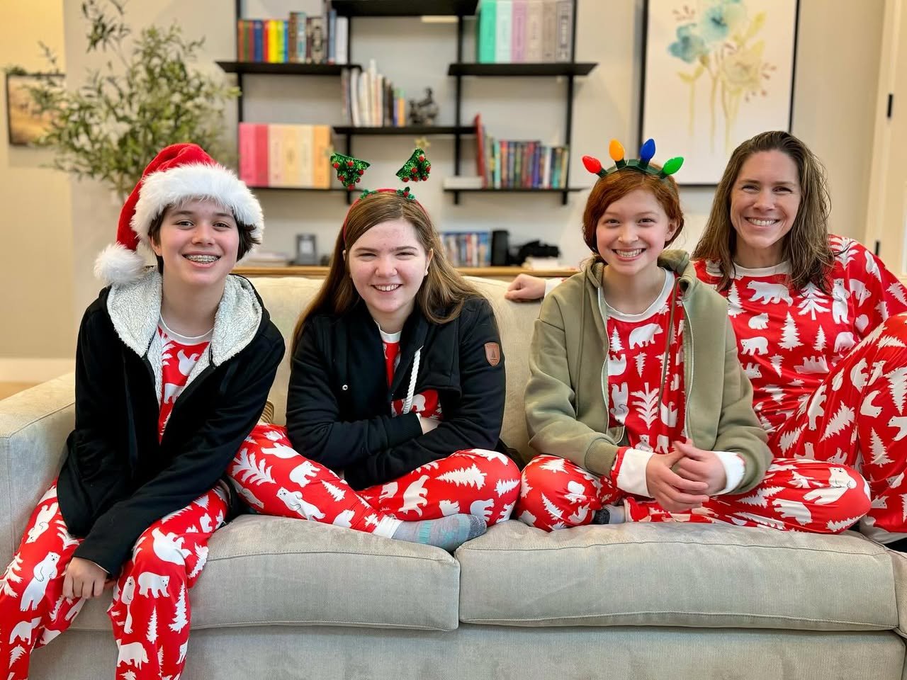 First Christmas at Bighorn & Bluebell A cozy family poses in matching red and white Christmas pajamas on the couch. One person wears a Santa hat while others have festive headbands with reindeer antlers and lights.