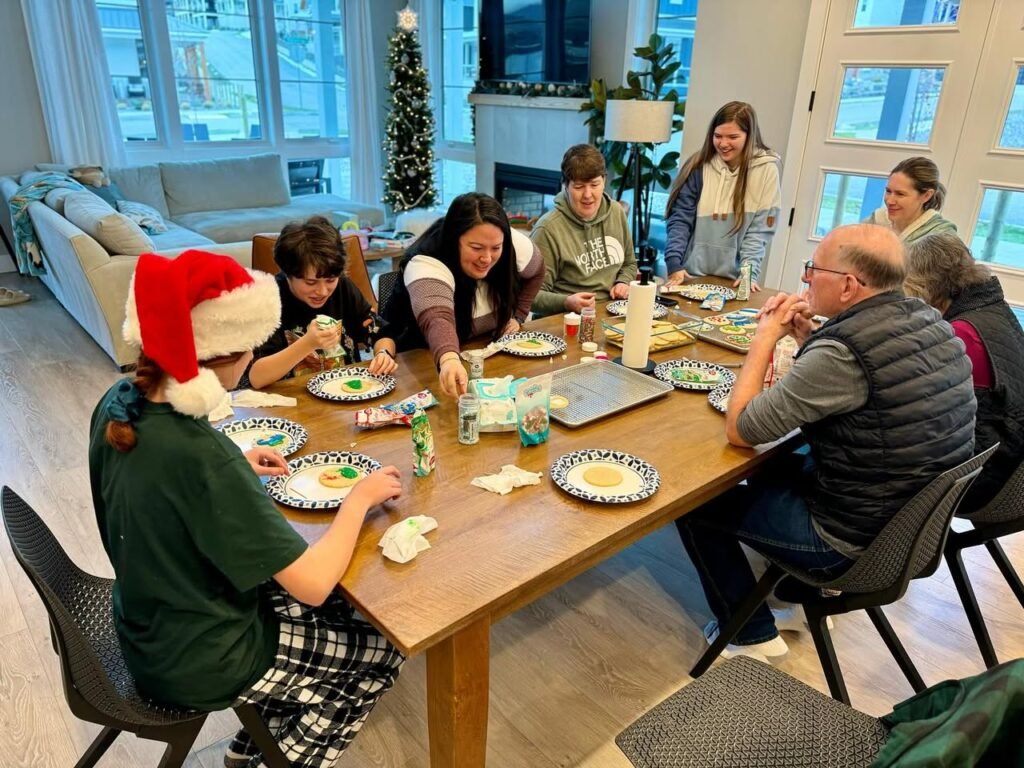 A group of people gathered around a large dining table decorated for the holidays with plates, crafts, and a Santa hat.