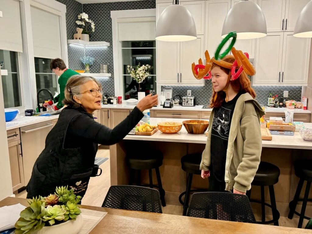 Family members in a cozy home kitchen during a festive celebration. One person wears a whimsical Halloween reindeer headband while others gather around the island with succulents and hanging pendant lights.
